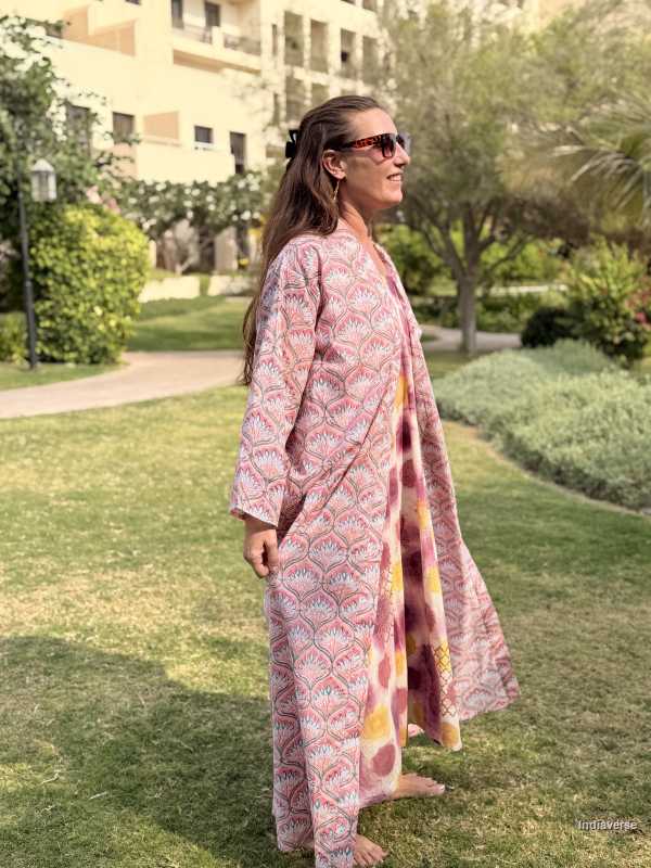 Woman in a pink patterned dress standing on grass with buildings and trees in the background
