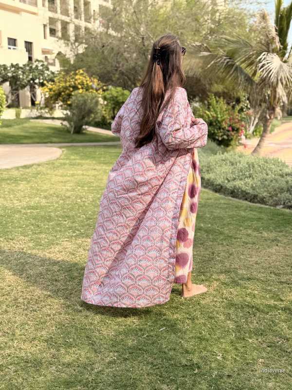 Woman in a patterned dress standing on grass with trees and buildings in the background