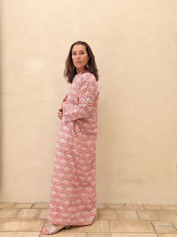 Woman wearing a pink patterned dress standing against a beige wall.