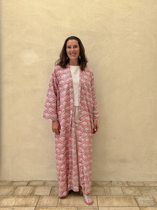 Woman wearing a pink patterned outfit standing against a beige wall.