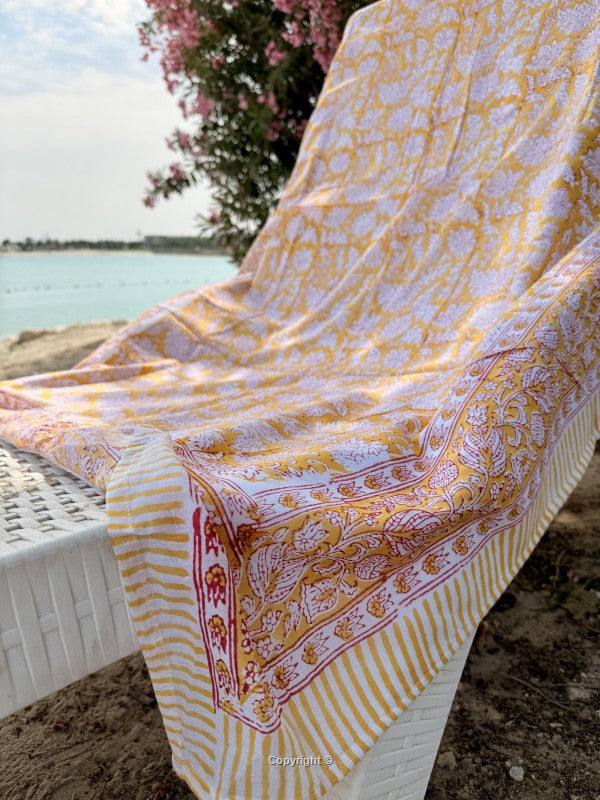 Yellow and white patterned blanket draped over a chair by a body of water.