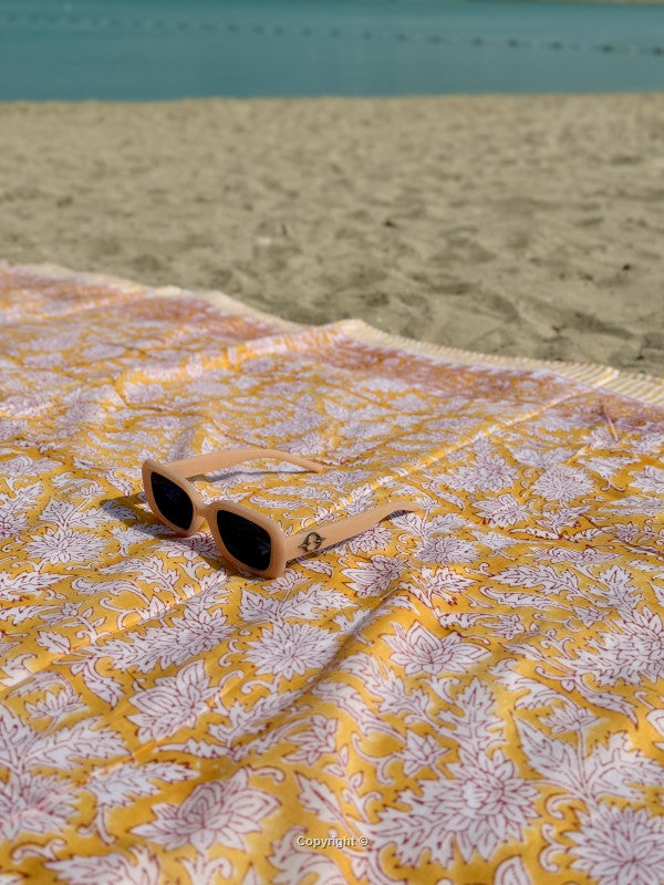 Beige sunglasses on a yellow and white patterned fabric with a beach background