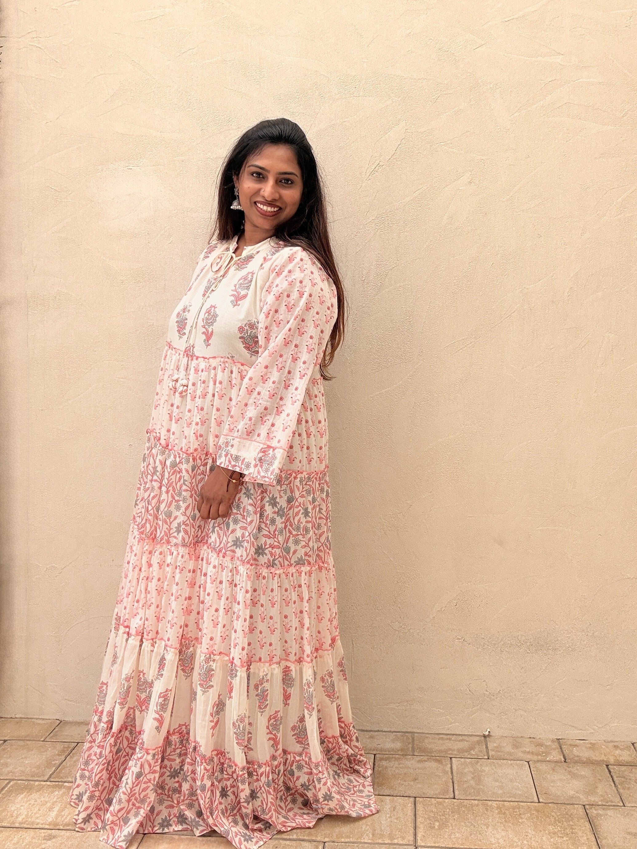 Woman wearing a floral dress standing against a beige wall.