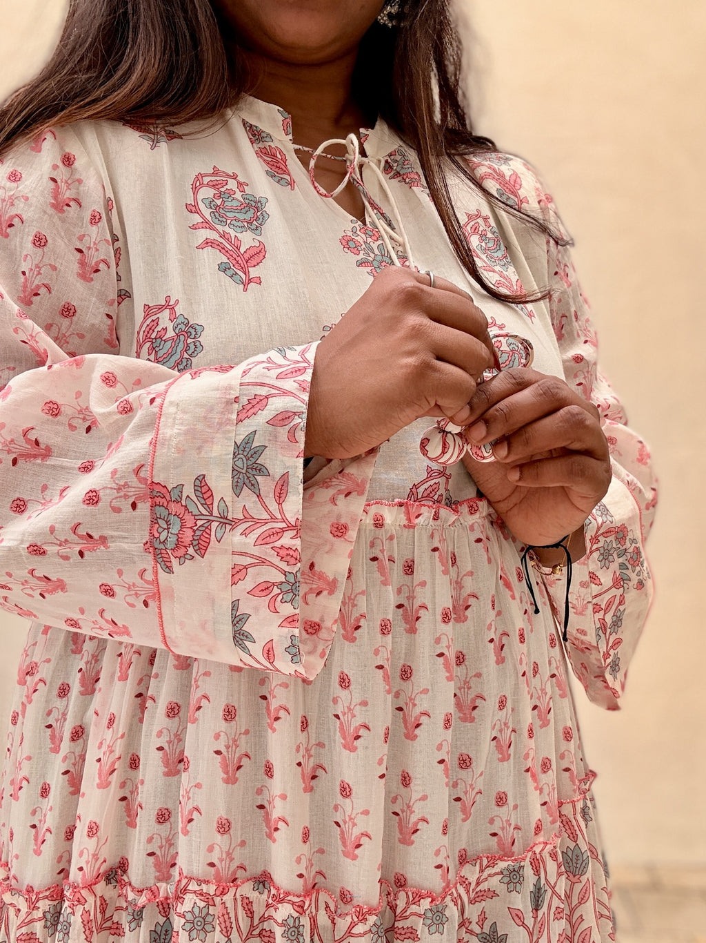 Person wearing a white dress with pink floral patterns against a beige background
