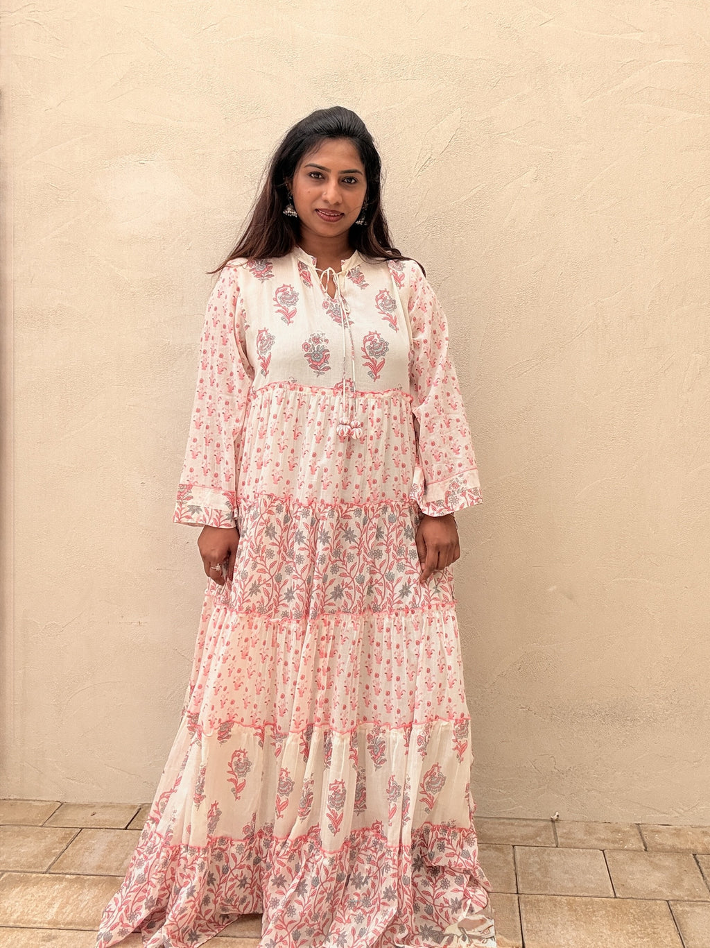 Woman wearing a floral dress standing against a beige wall.