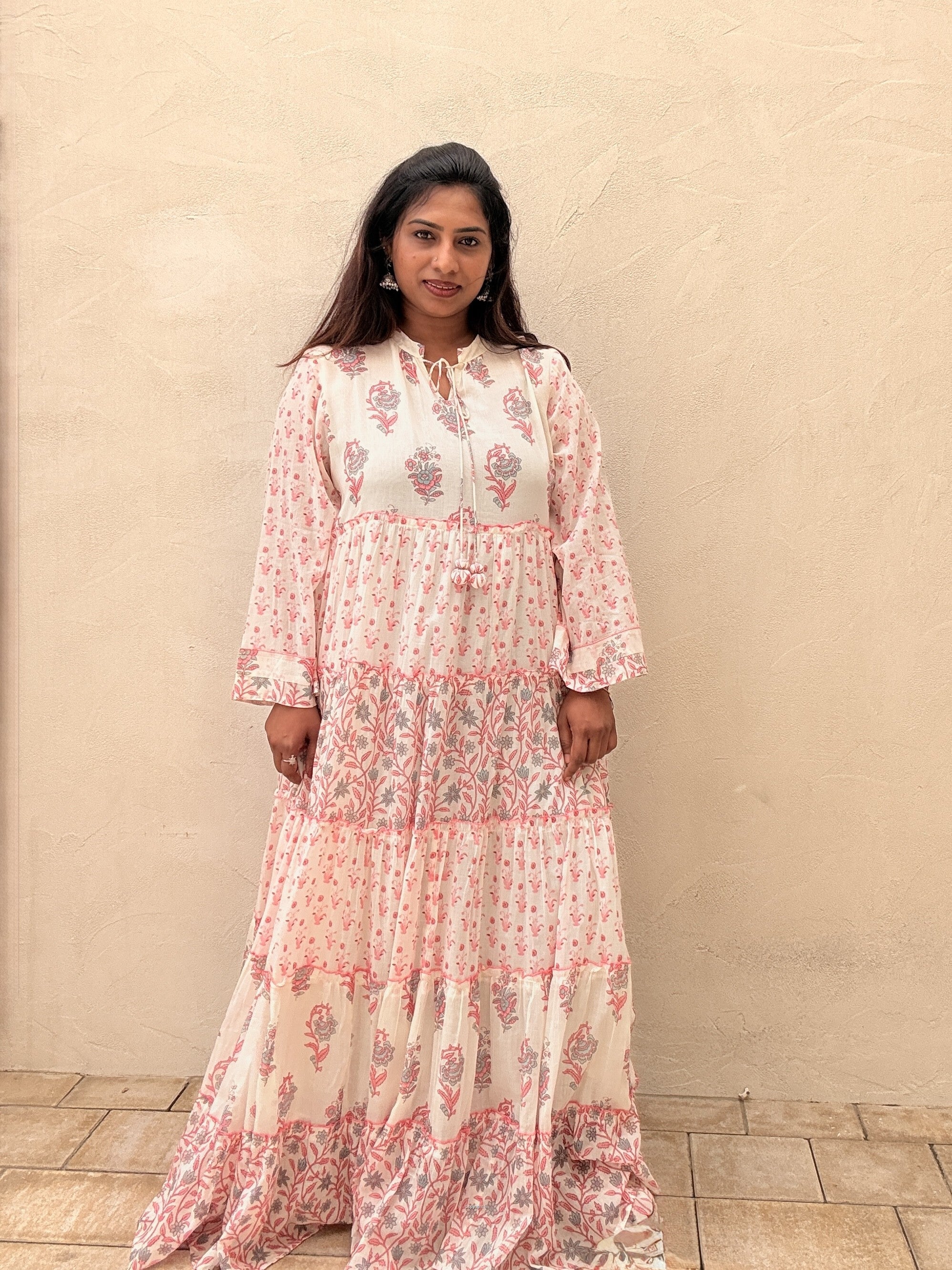 Woman wearing a floral dress standing against a beige wall.