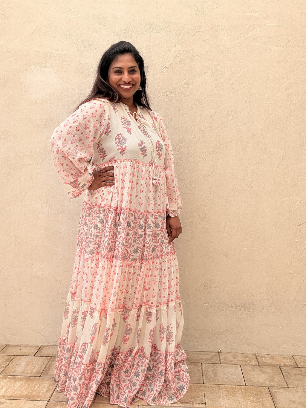 Woman wearing a floral dress standing against a beige wall.
