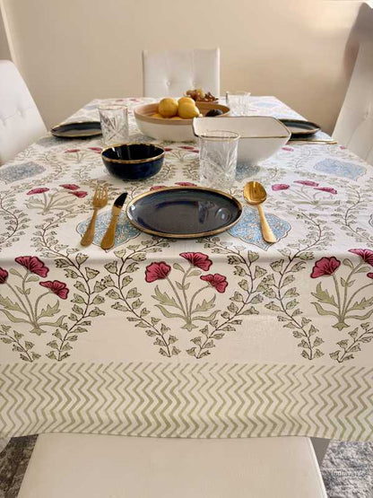 Dining table set with floral tablecloth, plates, cutlery, and glasses.