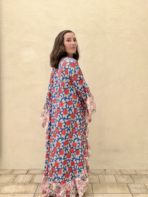 woman wearing a long kaftan dress with red rose design standing in front of a beige wall
