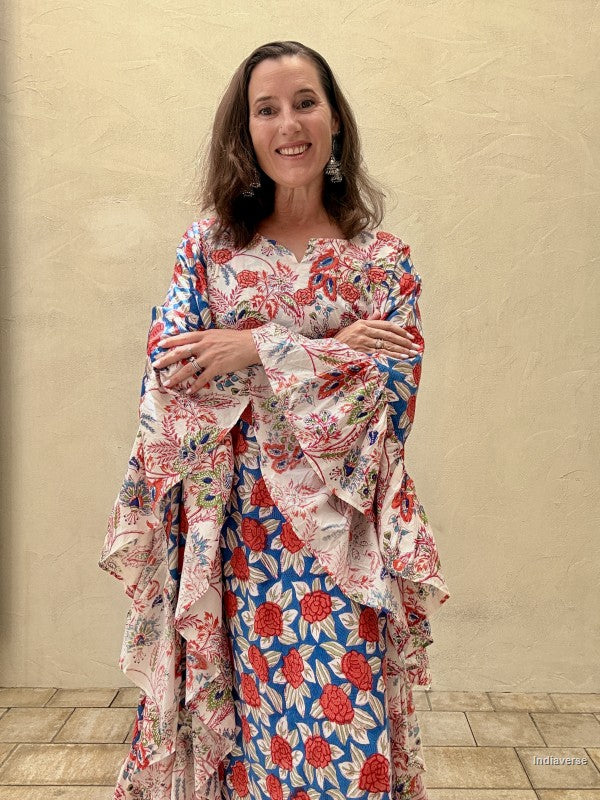 woman wearing a long floral kaftan dress with crossed arms standing in front of a beige wall