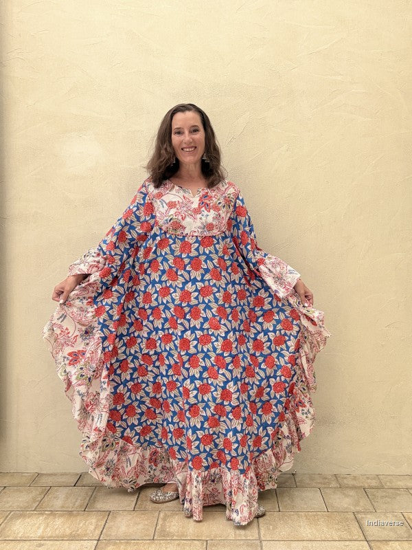 woman wearing a long kaftan dress with red rose design opening the skirt part wide standing in front of a beige wall