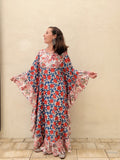 woman wearing a long kaftan dress with red rose design standing in front of a beige wall