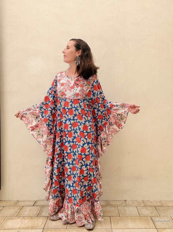 woman wearing a long kaftan dress with red rose design standing in front of a beige wall