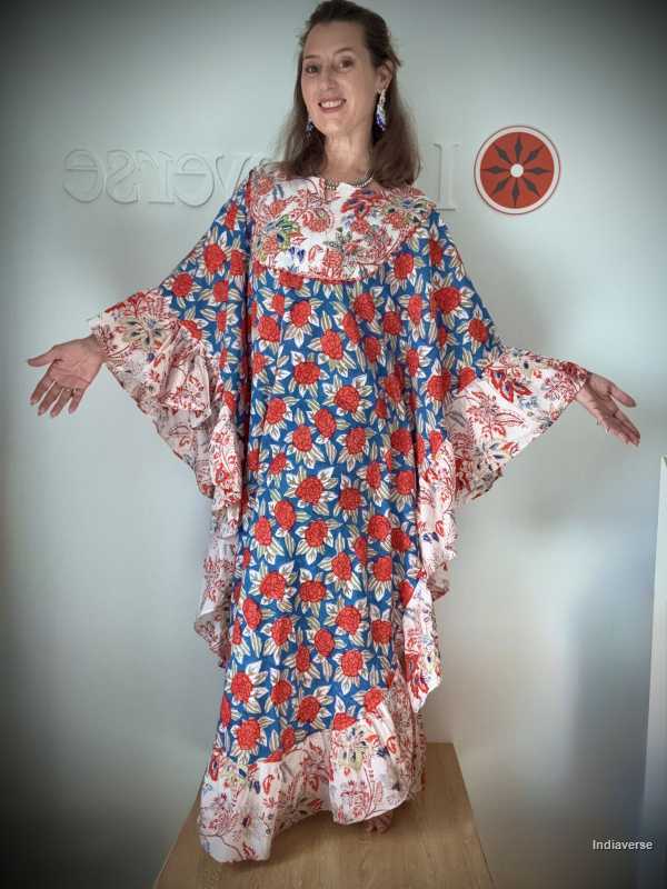 Woman wearing a colorful floral dress with arms outstretched against a plain background