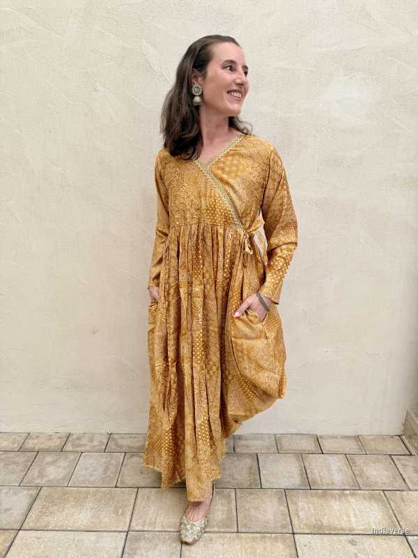 Woman wearing a yellow patterned dress standing against a beige wall.