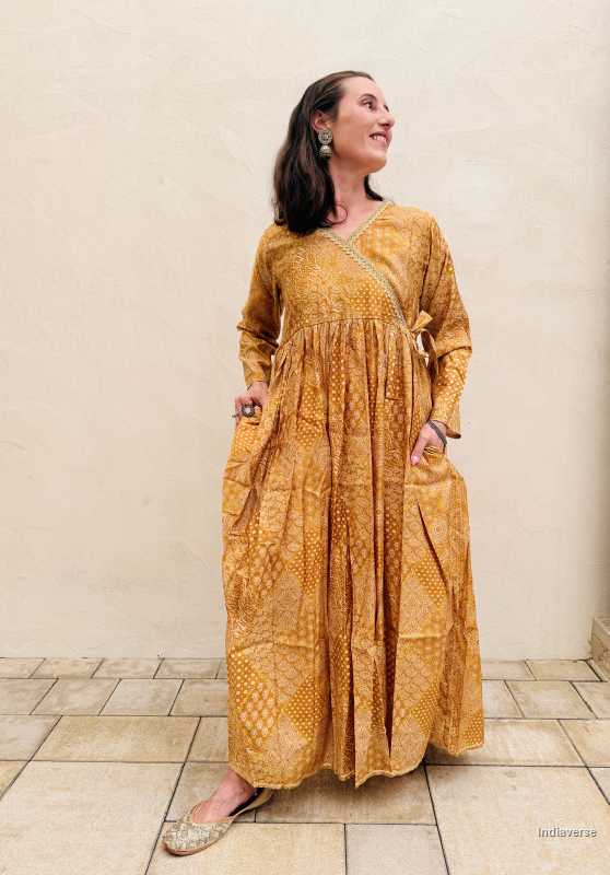 woman wearing a yellow golden maxi dress standing against a beige wall