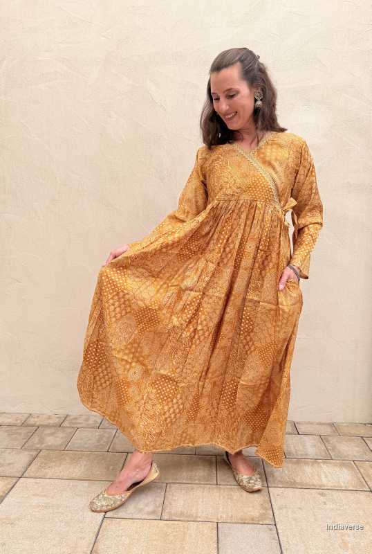 Woman wearing a long mustard yellow dress against a beige wall.