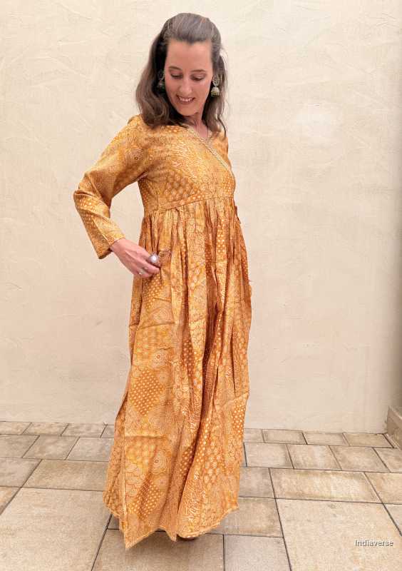Woman wearing a long yellow patterned dress against a beige wall.