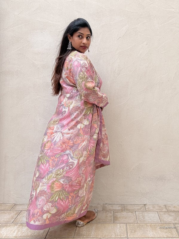 woman standing against a beige wall wearing a long maxi dress with pink and purple floral design