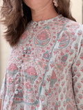 A close-up of a woman wearing a light beige tunic top with a detailed pink, teal, and white block print pattern and decorative buttons down the front.