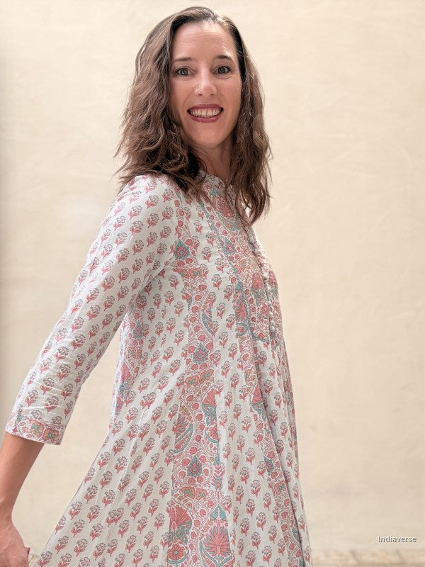 A woman wearing a three-quarter sleeve kurta with a pink and blue paisley pattern on a cream background, standing against a textured beige wall.