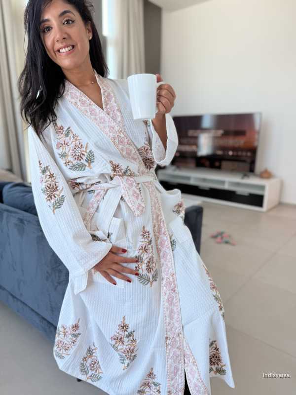 Woman in a floral robe holding a mug in a living room.