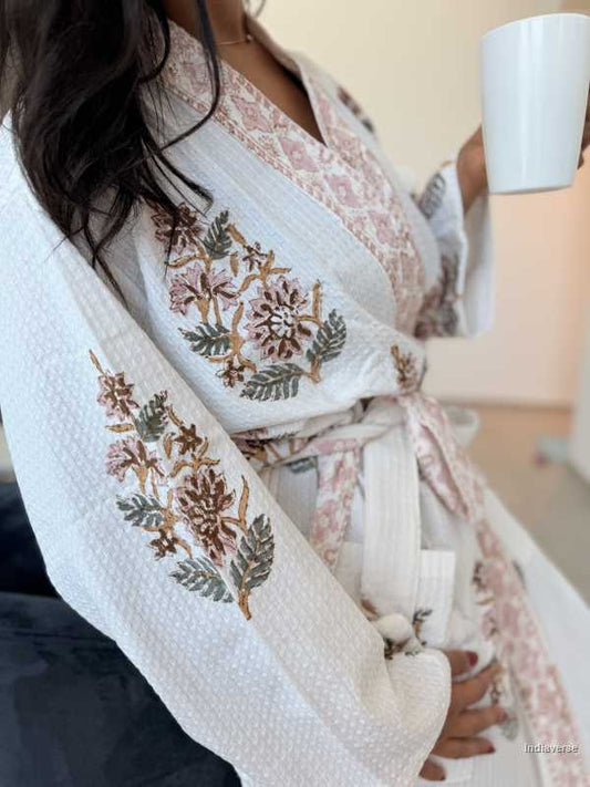 Person wearing a white kimono-style garment with floral embroidery, sitting indoors.