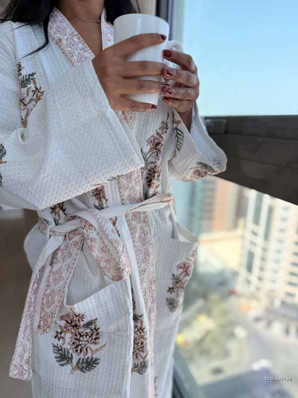 Person wearing a floral embroidered robe holding a cup by a window with cityscape view