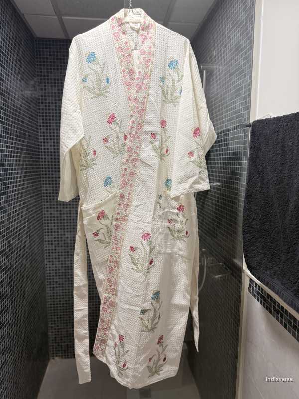 Embroidered robe hanging on a hook in a tiled bathroom.