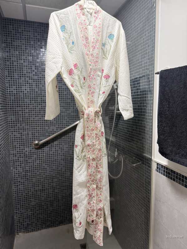 Floral-patterned bathrobe hanging on a hook in a tiled bathroom.