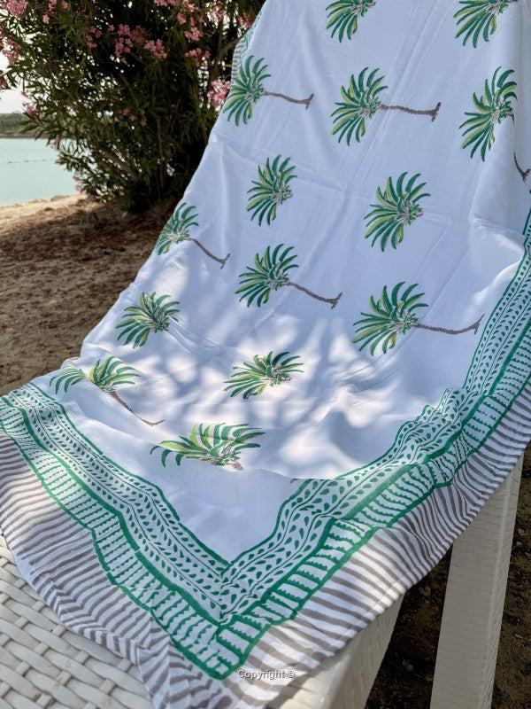 White towel with green palm tree patterns draped over a chair by a body of water.