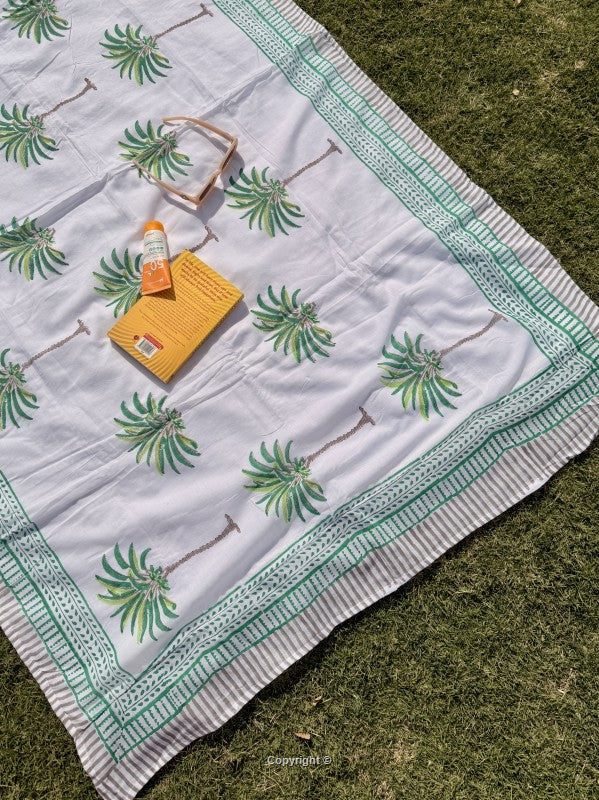 White blanket with green palm tree patterns on grass