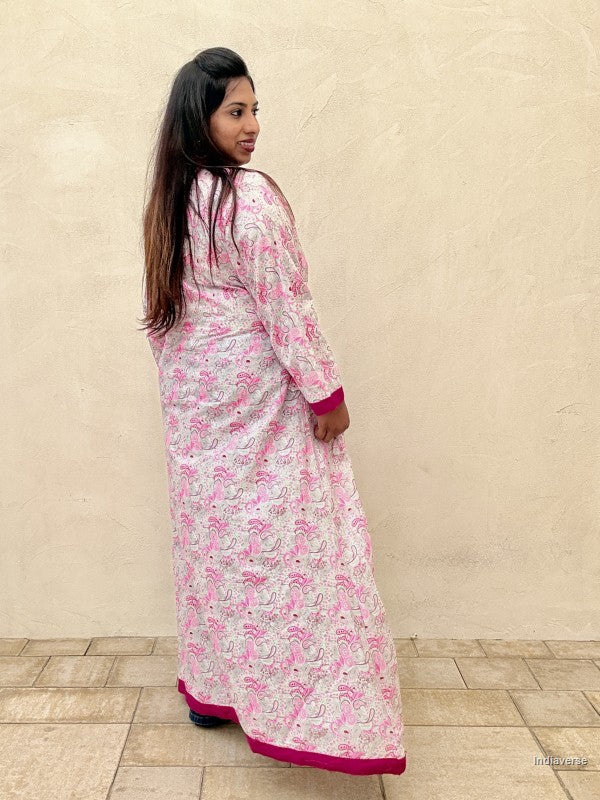 Woman wearing a long floral dress with pink accents against a beige wall.