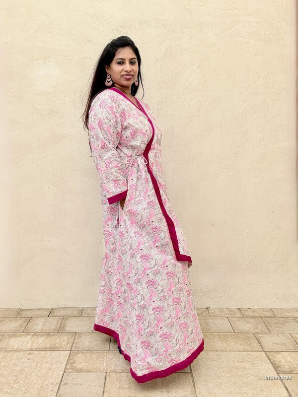 Woman wearing a pink and white floral dress with a red border against a beige wall.