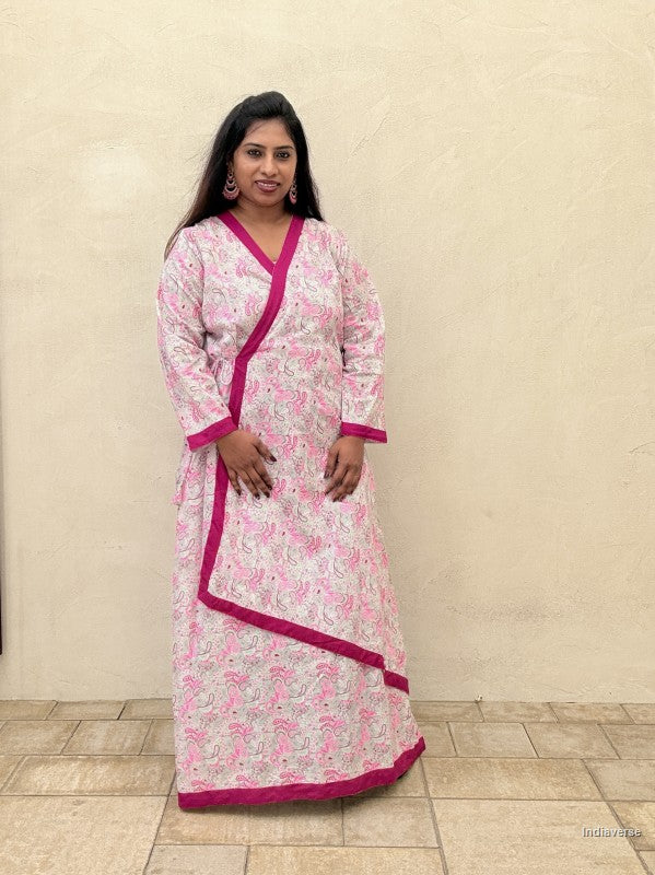 Woman wearing a pink and white patterned dress with a matching dupatta against a beige wall.