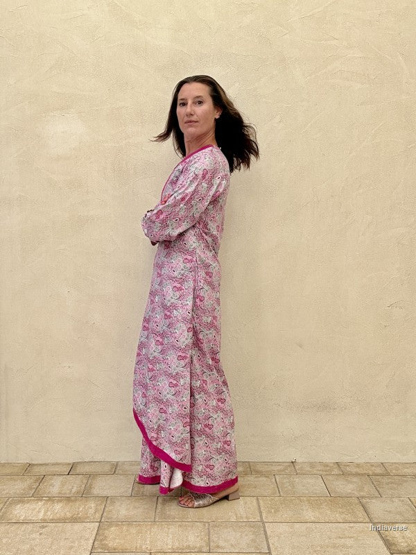 Woman wearing a pink floral dress standing against a beige wall.