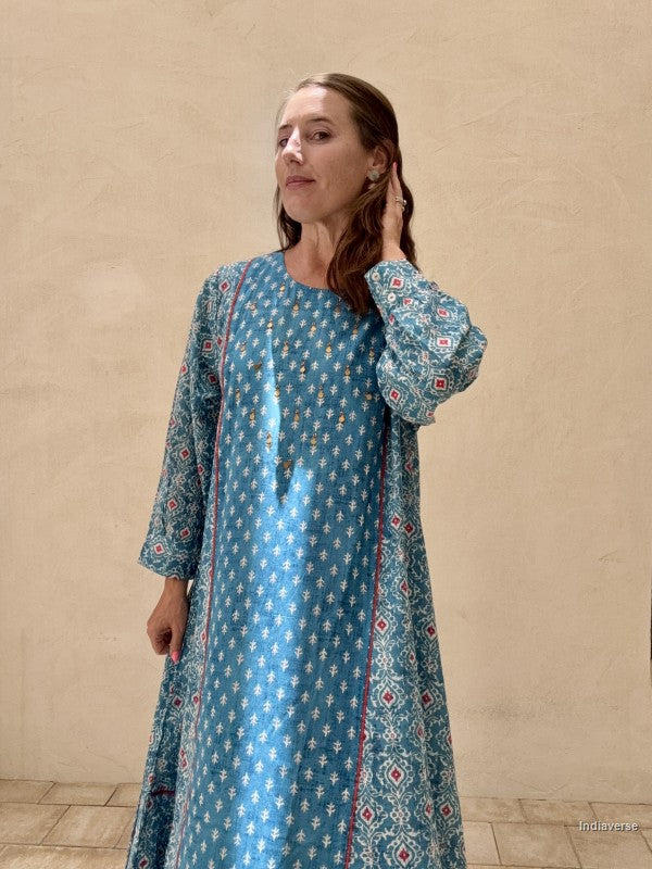 Woman wearing a blue patterned dress against a beige wall.