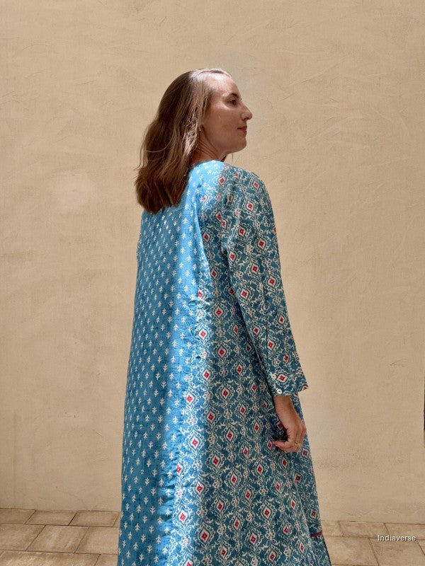 Woman wearing a blue patterned dress against a beige wall.