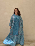 Woman wearing a blue patterned dress standing against a beige wall.
