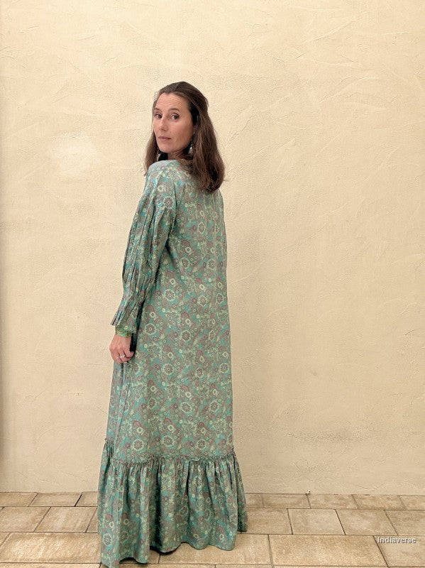 Woman wearing a green patterned dress standing against a beige wall.
