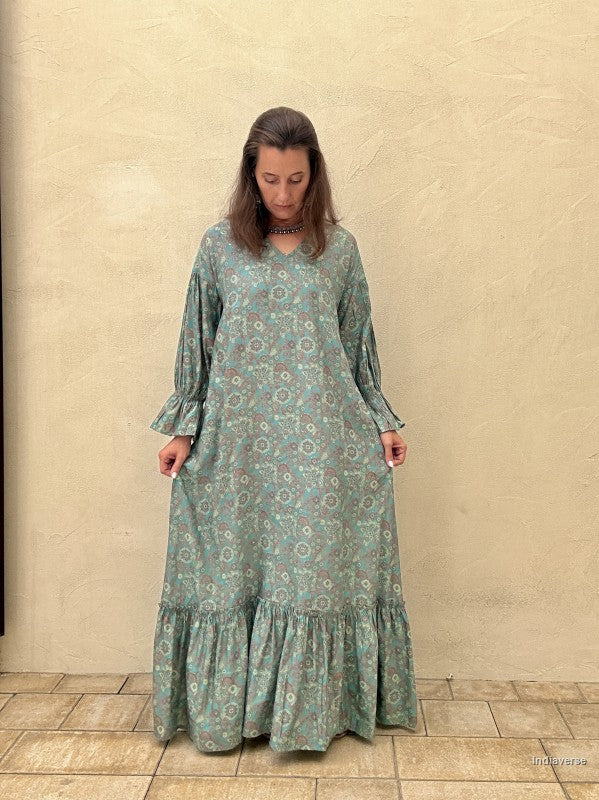 Woman wearing a long green floral dress against a beige wall.