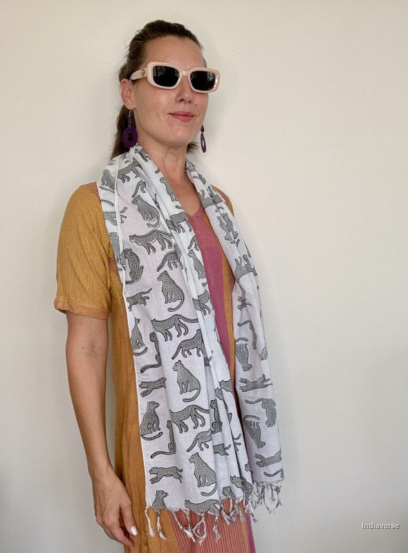 Woman wearing a patterned scarf and sunglasses against a plain background
