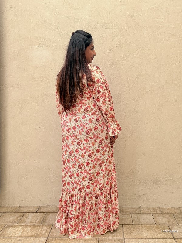 Woman wearing a red floral long dress standing facing a beige wall