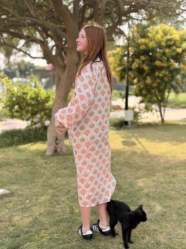 Woman in a floral dress standing with a black cat on grass
