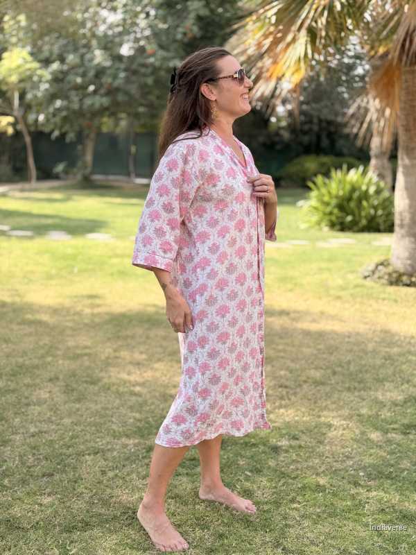 Woman wearing a pink floral dress standing on grass with trees in the background