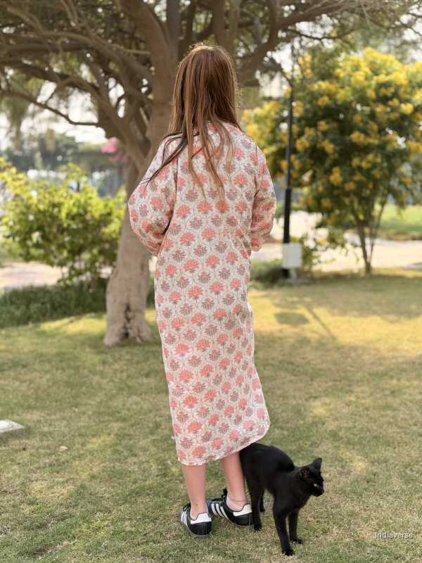 Person in a floral dress standing with a black cat on grass