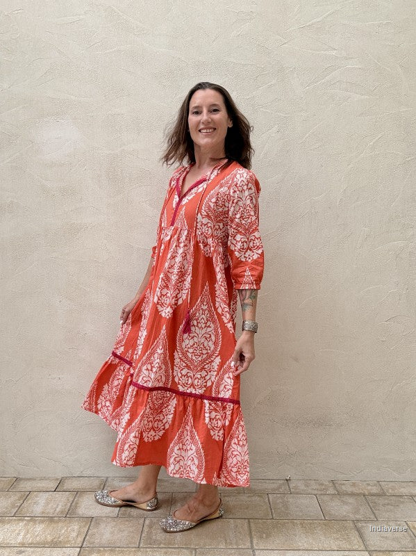 Woman wearing a red and white patterned dress standing against a beige wall.