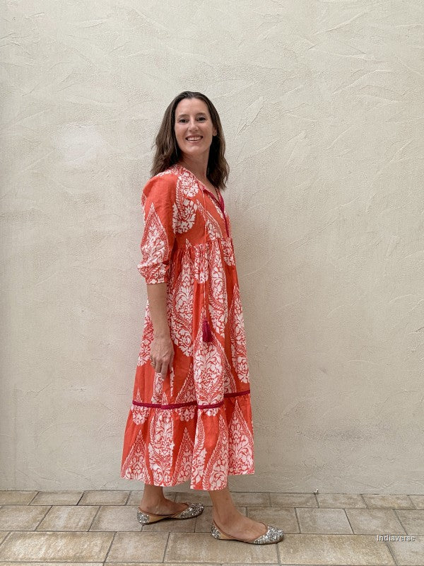 Woman wearing a red and white patterned dress standing against a beige wall.
