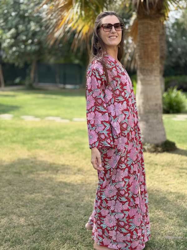 Woman wearing a pink floral dress standing in a park with trees and grass.