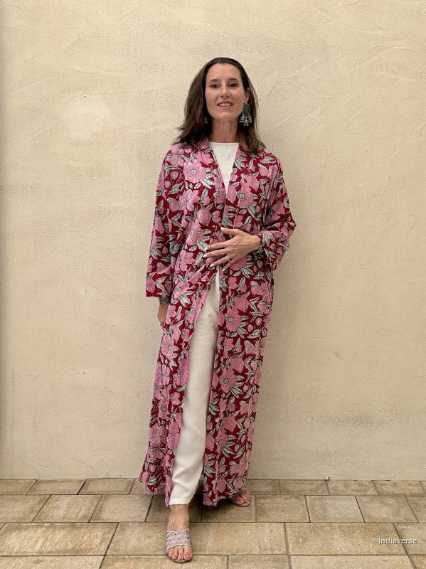 Woman wearing a pink floral outfit standing against a beige wall.